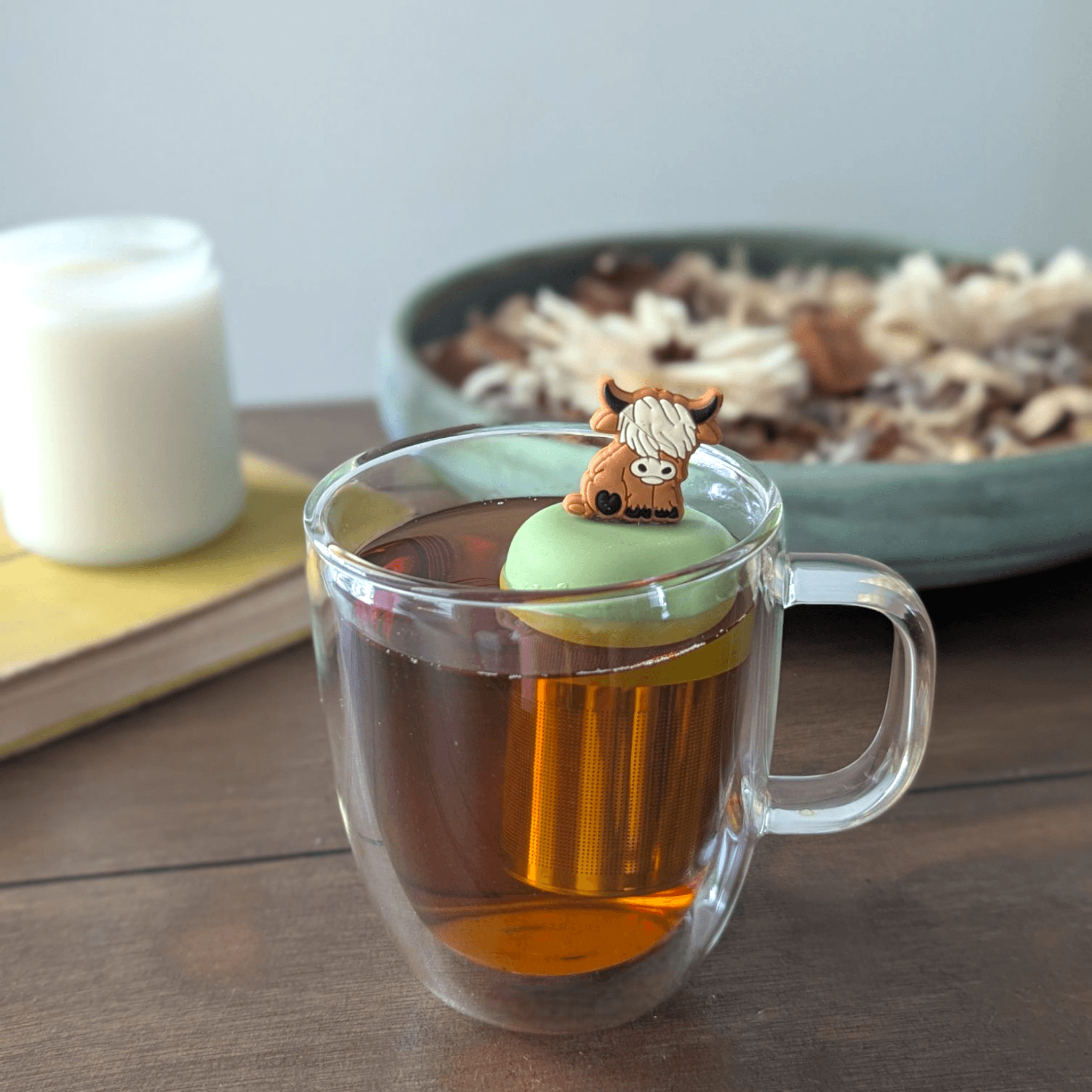 Floating Adult Highland Cow Tea Infuser in a clear mug of tea with a green lid, perfect for loose leaf tea.
