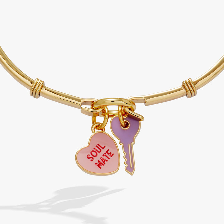 Gold bangle with heart-shaped 'Soul Mate' charm and purple key charm on a white background